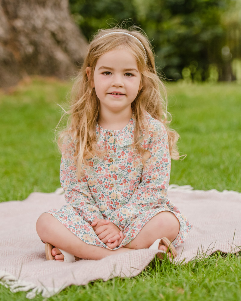 young girl sat on blanket in Summer wearing flowery dress and pearl headband
