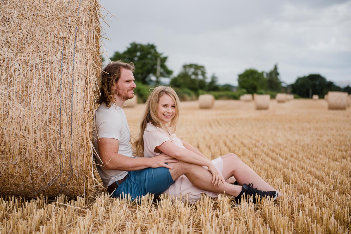 bride and groom to be sitting in wheat field on photoshoot with Victoria La Bouchardiere in Shropshire