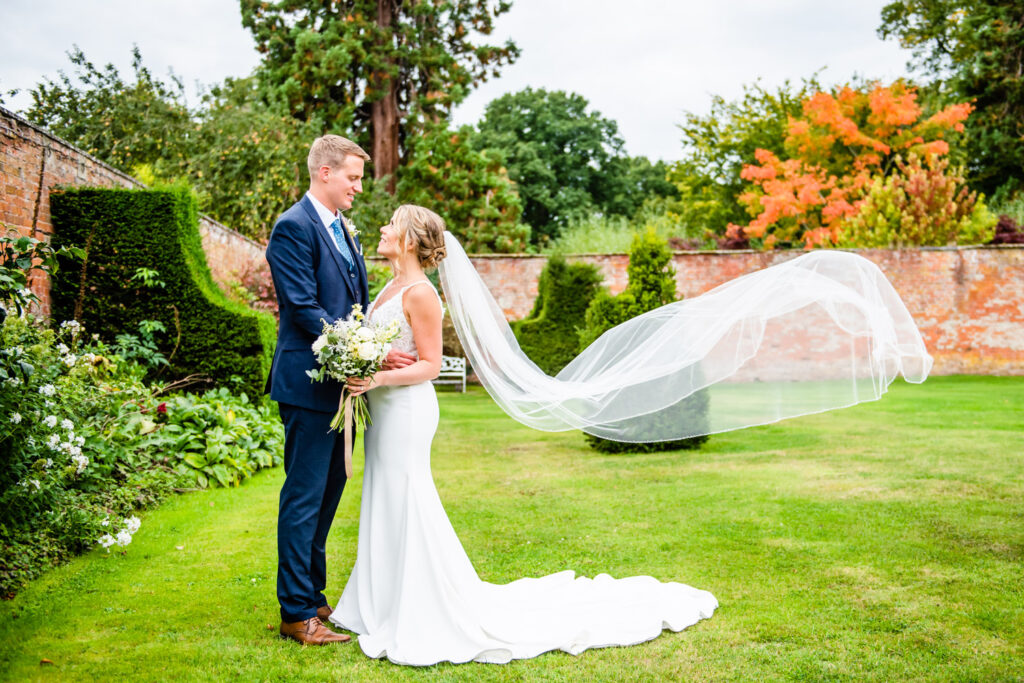 groom holding bride with veil floating in walled garden at Comermere Abbey wedding venue with Victoria La Bouchardiere